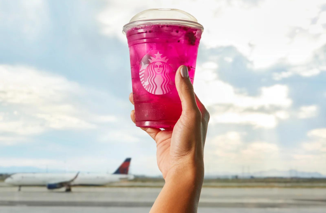 person holding up starbucks drink with plane in the background