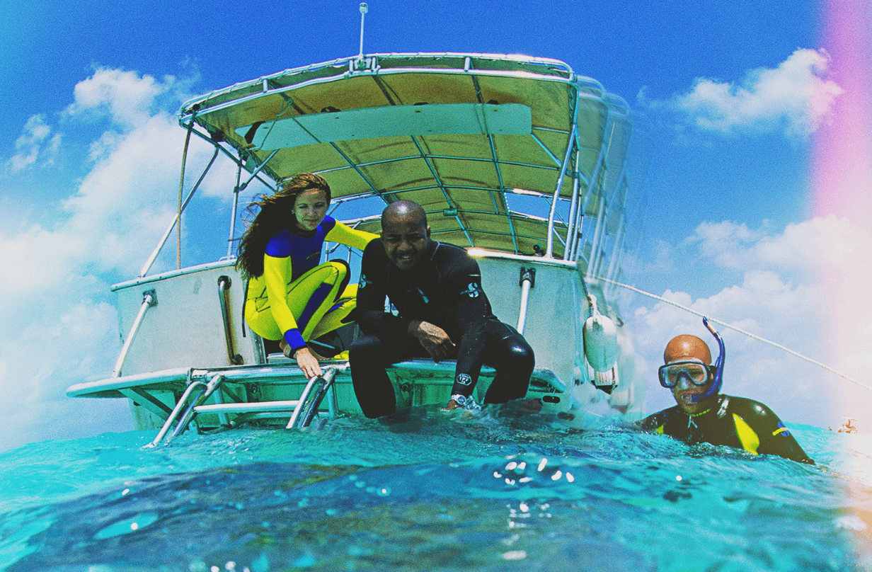 couple sitting on back of boat with snorkel instructor in water