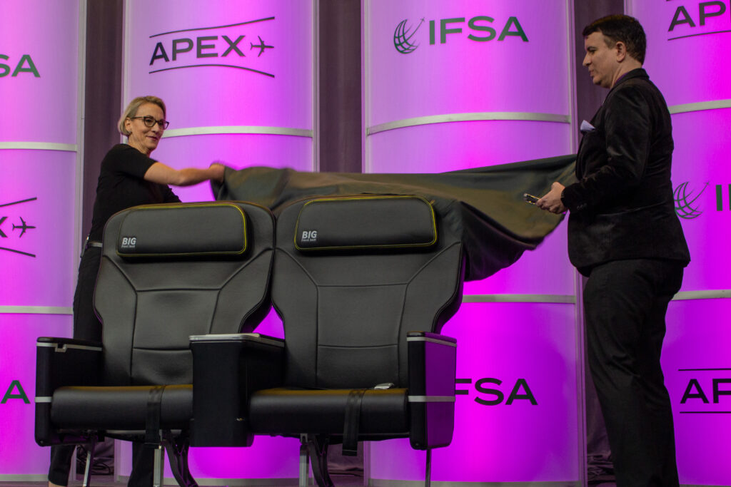 a man and a woman pull a black tarp off to unveil Spirit Airlines' new Big Front Seats at an event