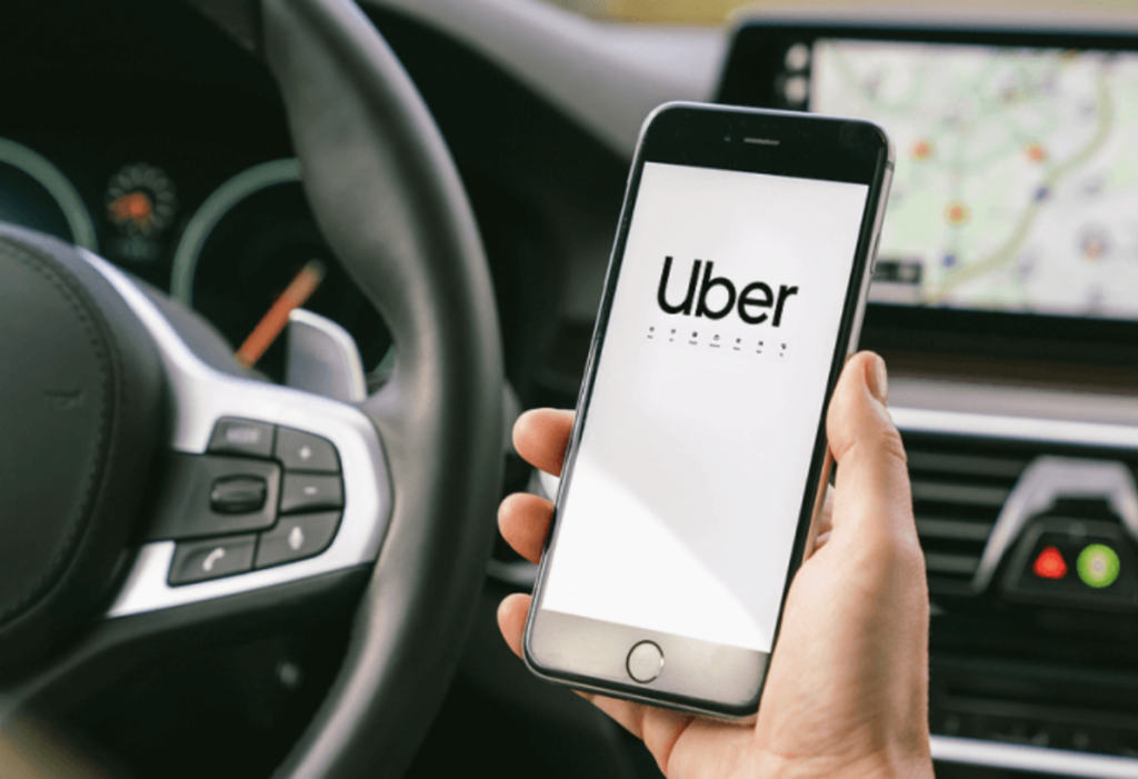 person driving with phone in their hand, with uber app displayed