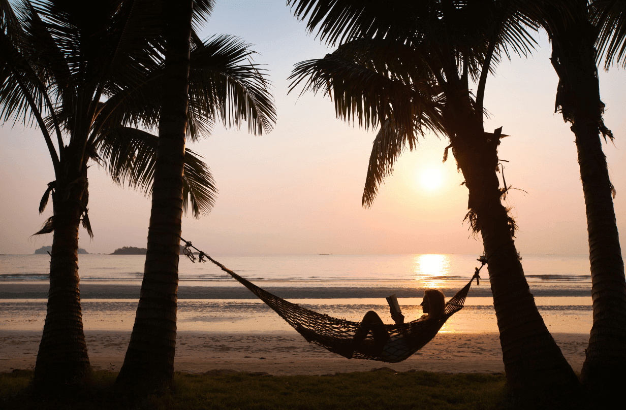 person lounging on hammock during sunset between two palm trees