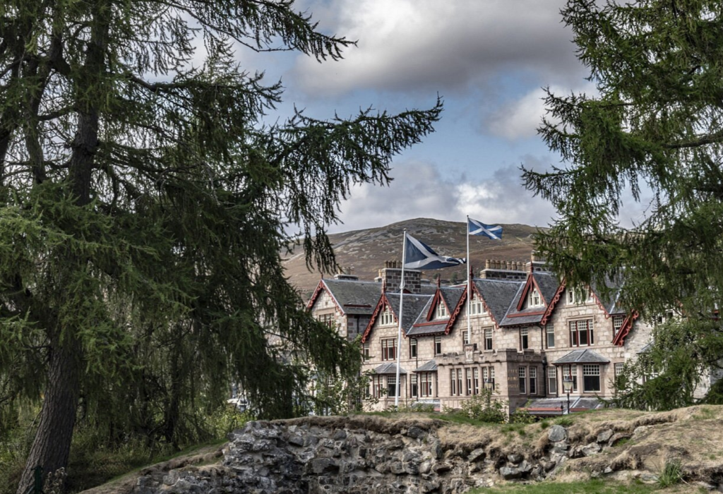 Exterior of The Fife Arms from a distance with trees, rocks, and the hotel building in view