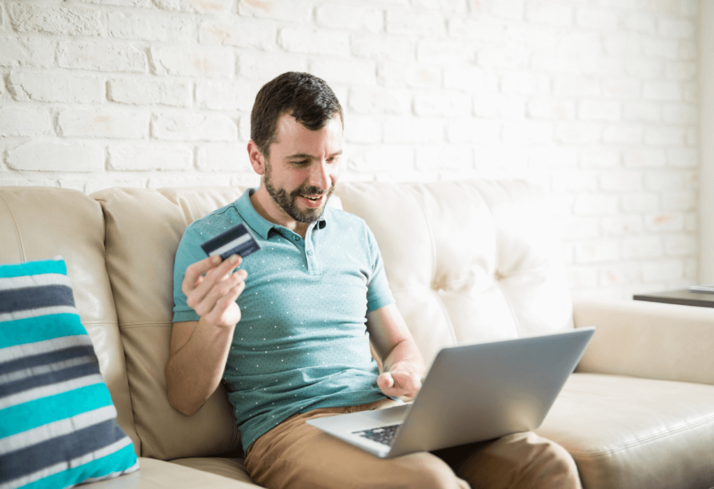 man holding credit card sitting on couch with laptop
