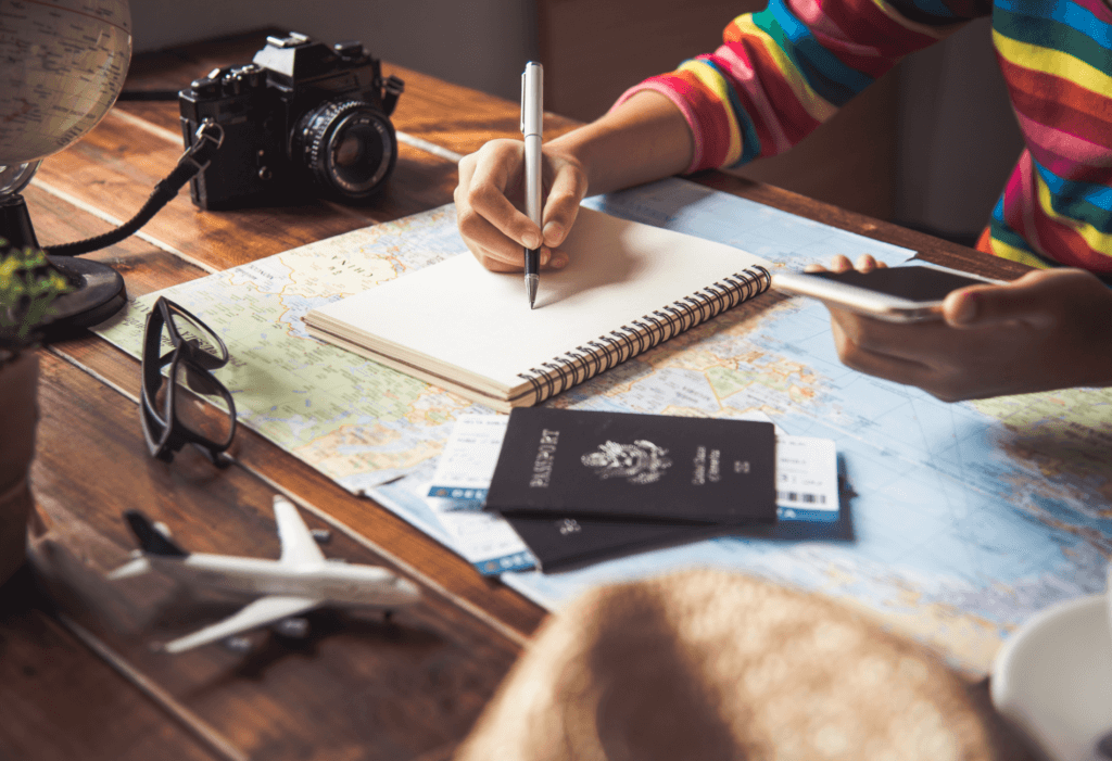 person writing in notebook with passport and map nearby