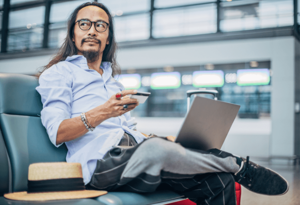 man with credit card and laptop at airport, for article on how to choose a bank