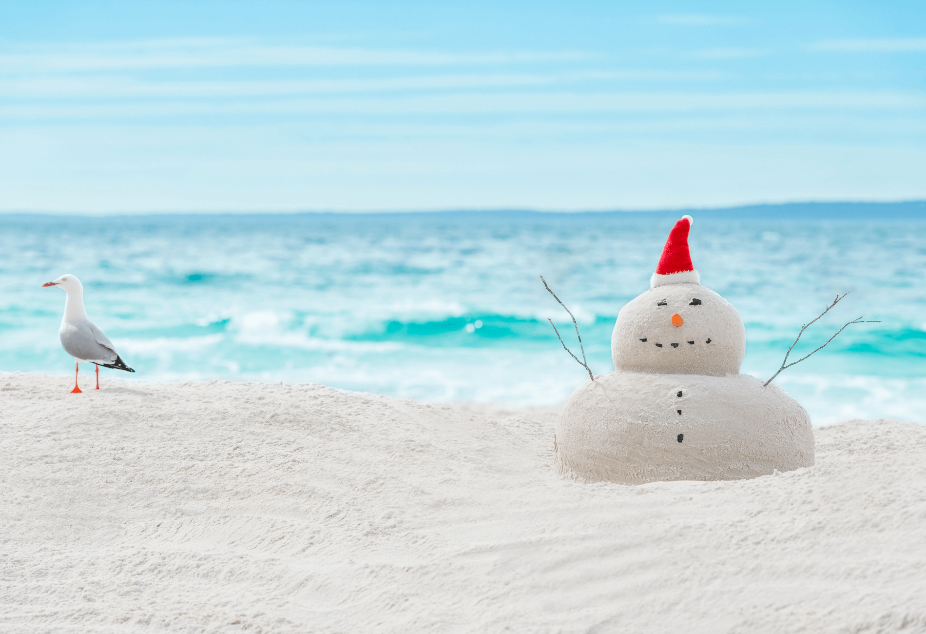snowman made of sand on beach with turquoise waters
