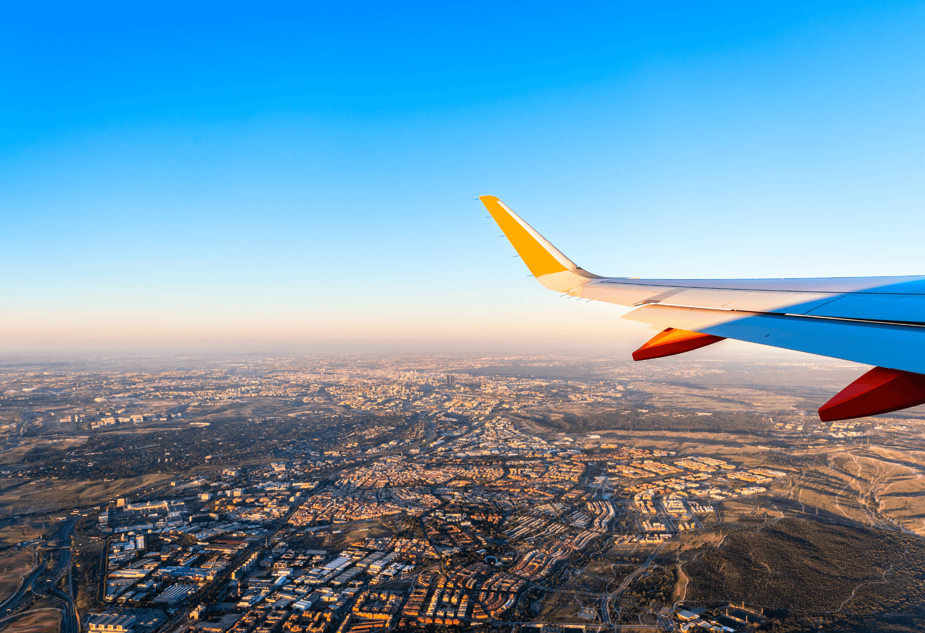 plane wing shown above cityscape for article on Southwest flash sale and deals you can get using the low fare calendar
