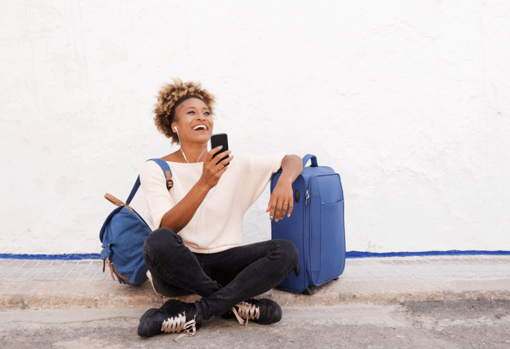 woman holding cell phone laughing while sitting on the ground holding luggage