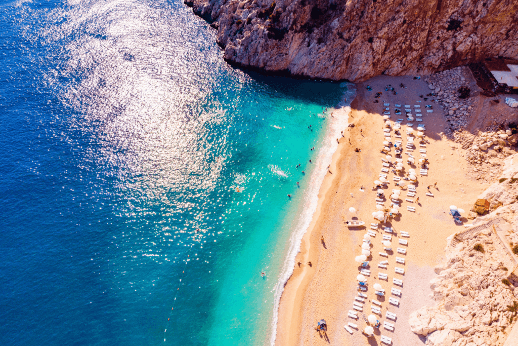 A view from above of a Turkish Riviera beach with blue water, golden sand and large cliffs