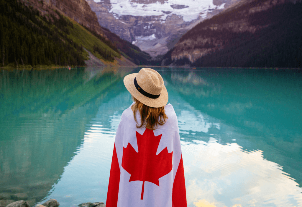 A girl standing by a lake in Banff national park with a Canadian flag around her